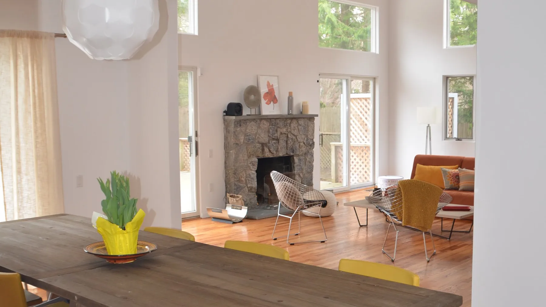 A bright open-plan living and dining area with tall windows and colorful seating.