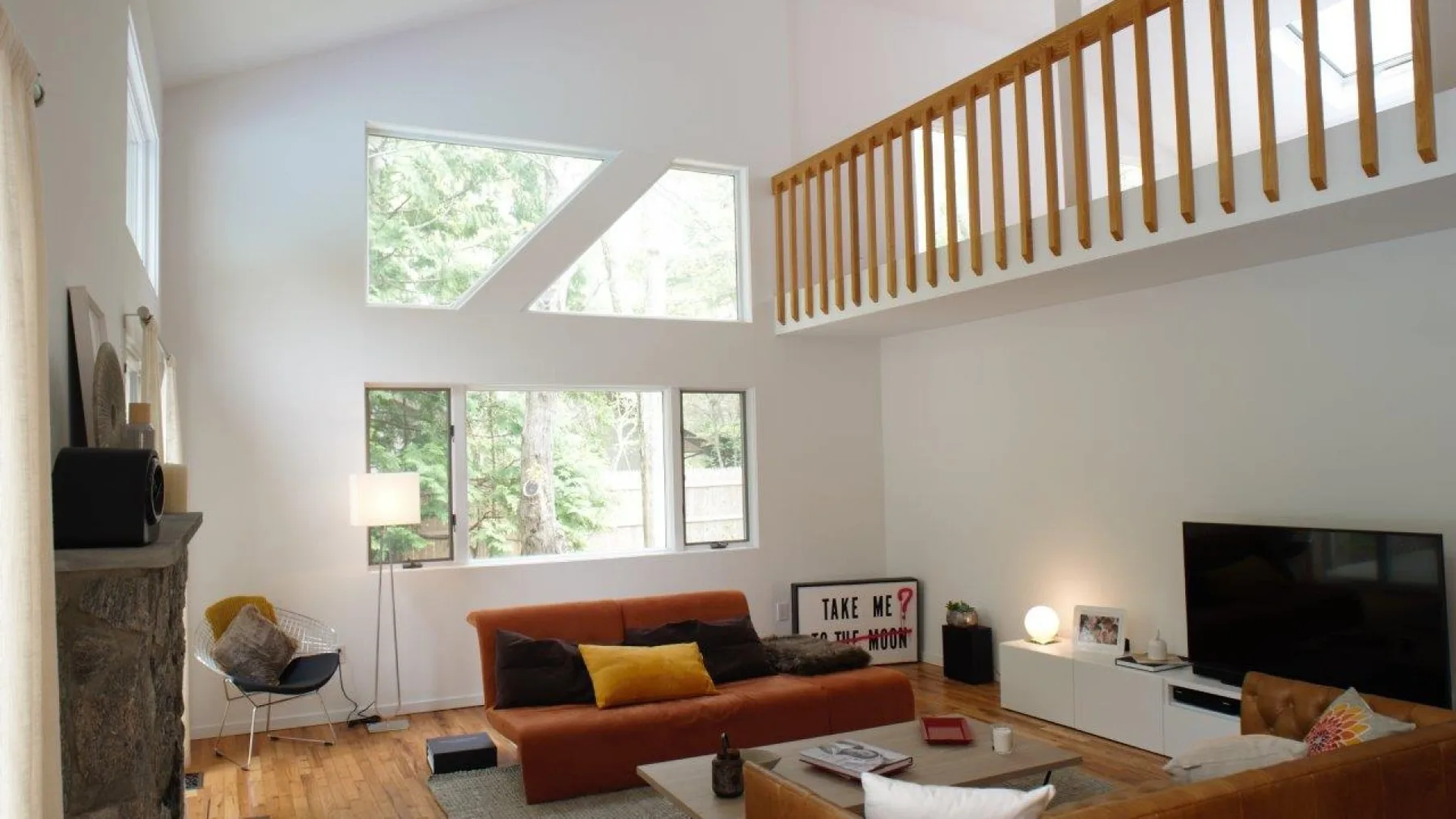A bright living room with a sectional sofa, television, and wooden upper railing.