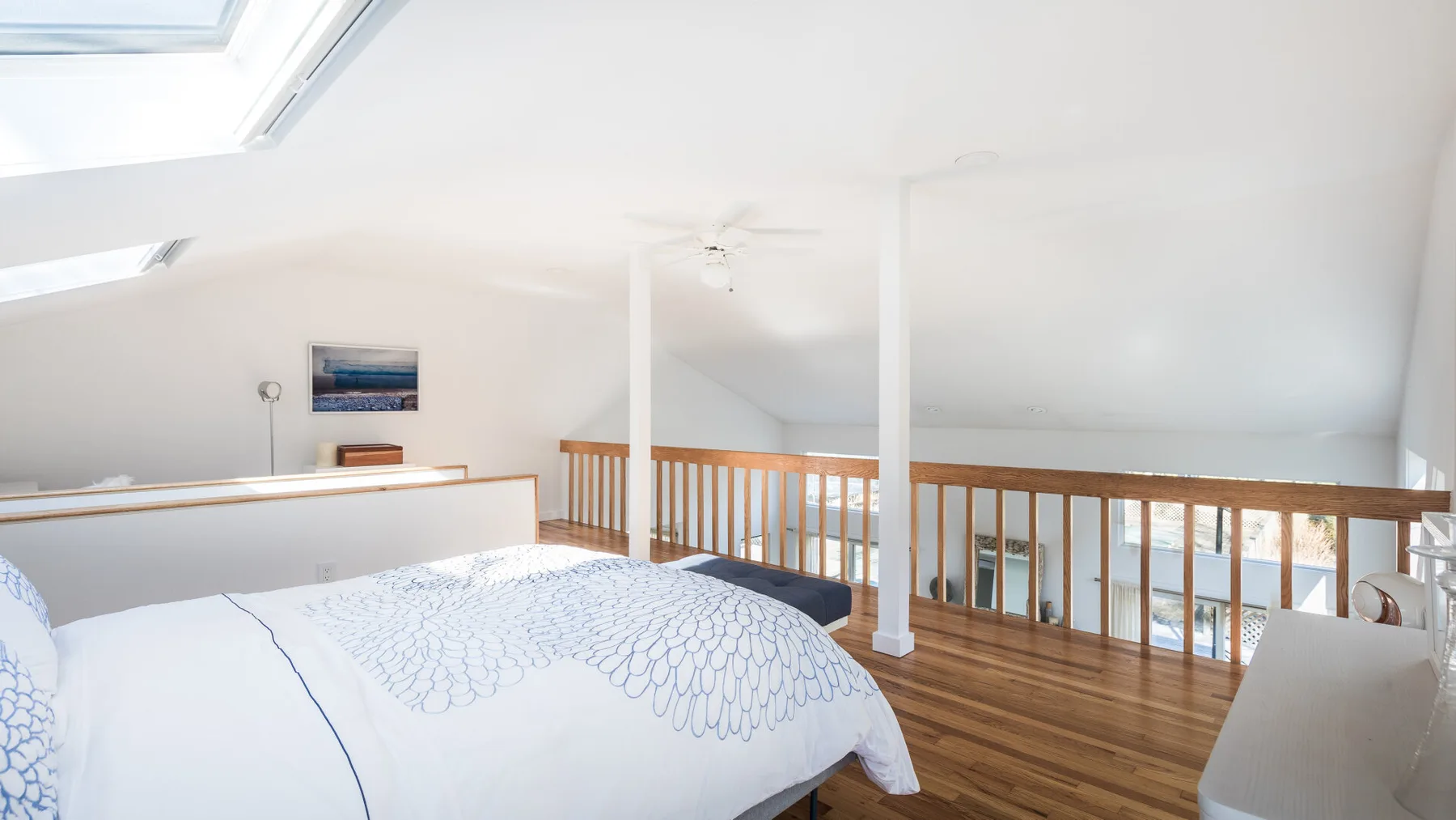 Un dormitorio tipo loft luminoso, con una cama bajo un techo inclinado y una barandilla de madera.
