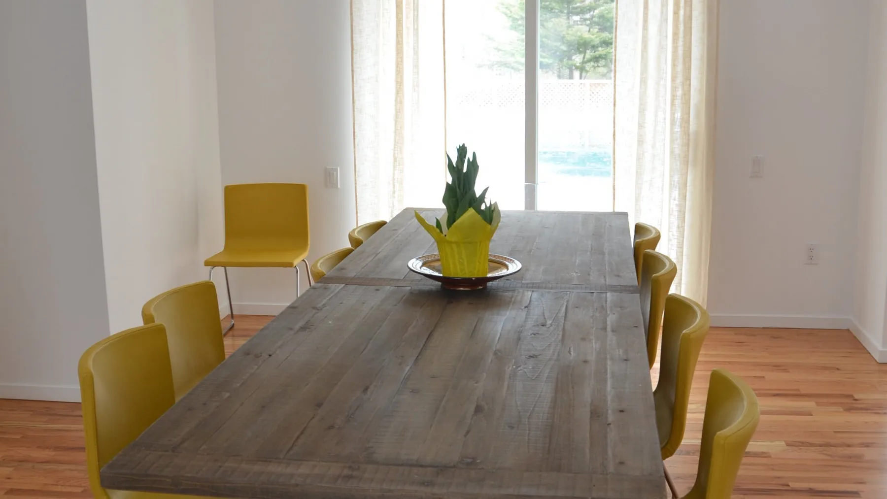 Comedor con una mesa larga de madera, asientos amarillos y un centro de mesa con plantas.