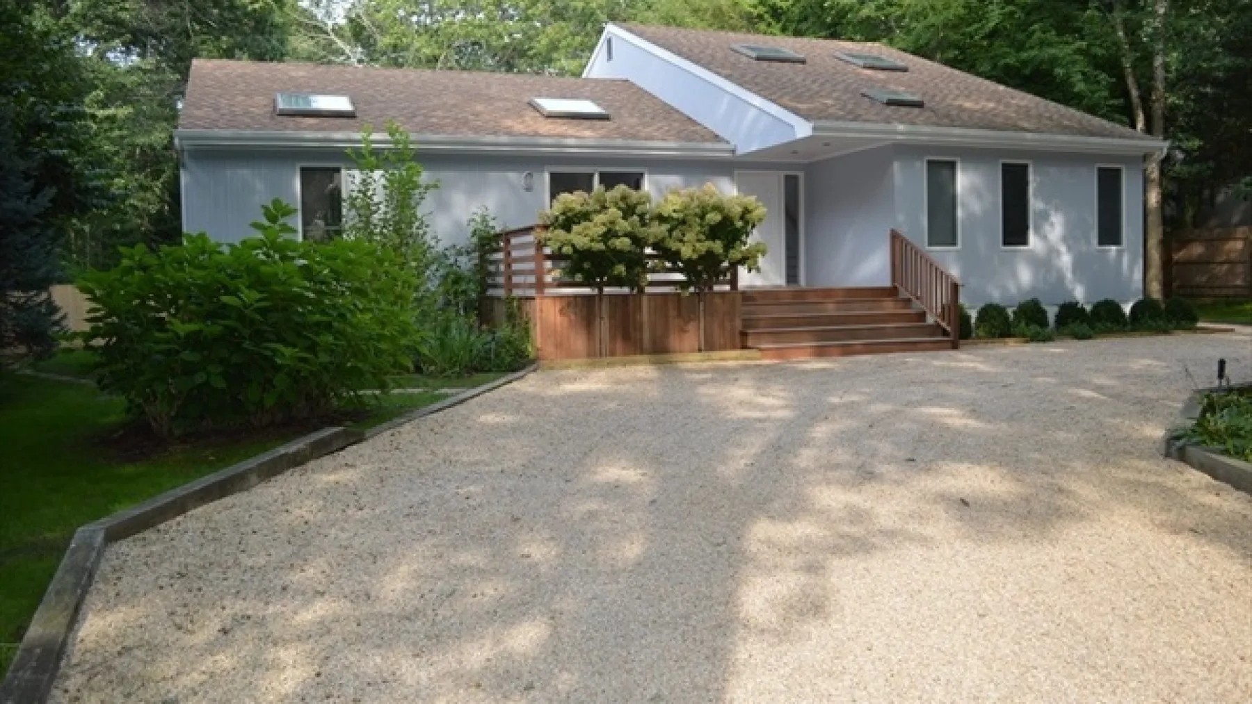 A gray house with a broad gravel driveway and steps leading to the entrance.