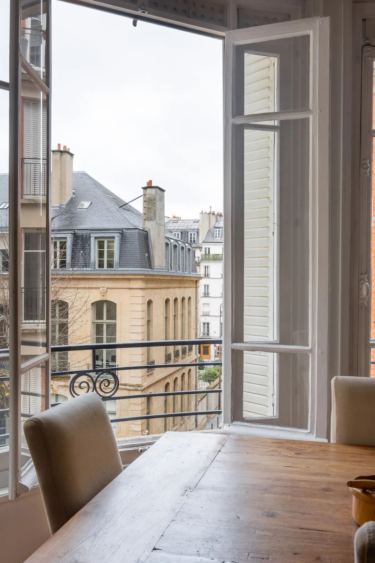 Un comedor junto a una ventana abierta tiene vistas a edificios cercanos.