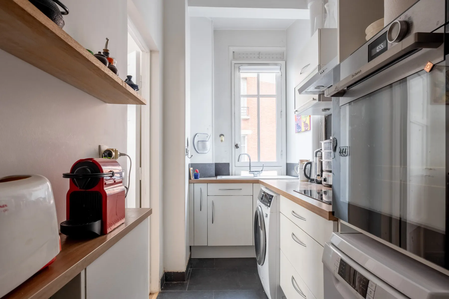 Una cocina estrecha con electrodomésticos integrados y una ventana al fondo.