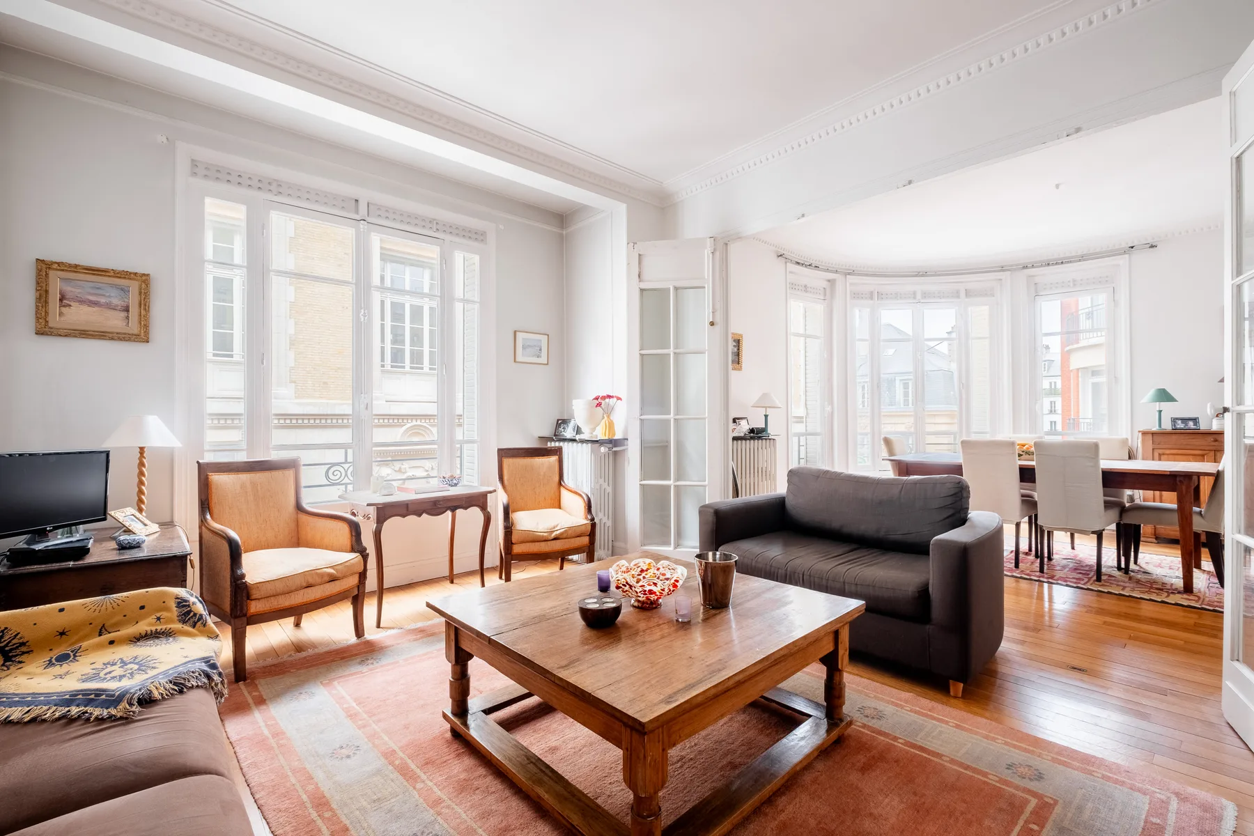 Una sala luminosa con asientos alrededor de una mesa de centro de madera y grandes ventanas.