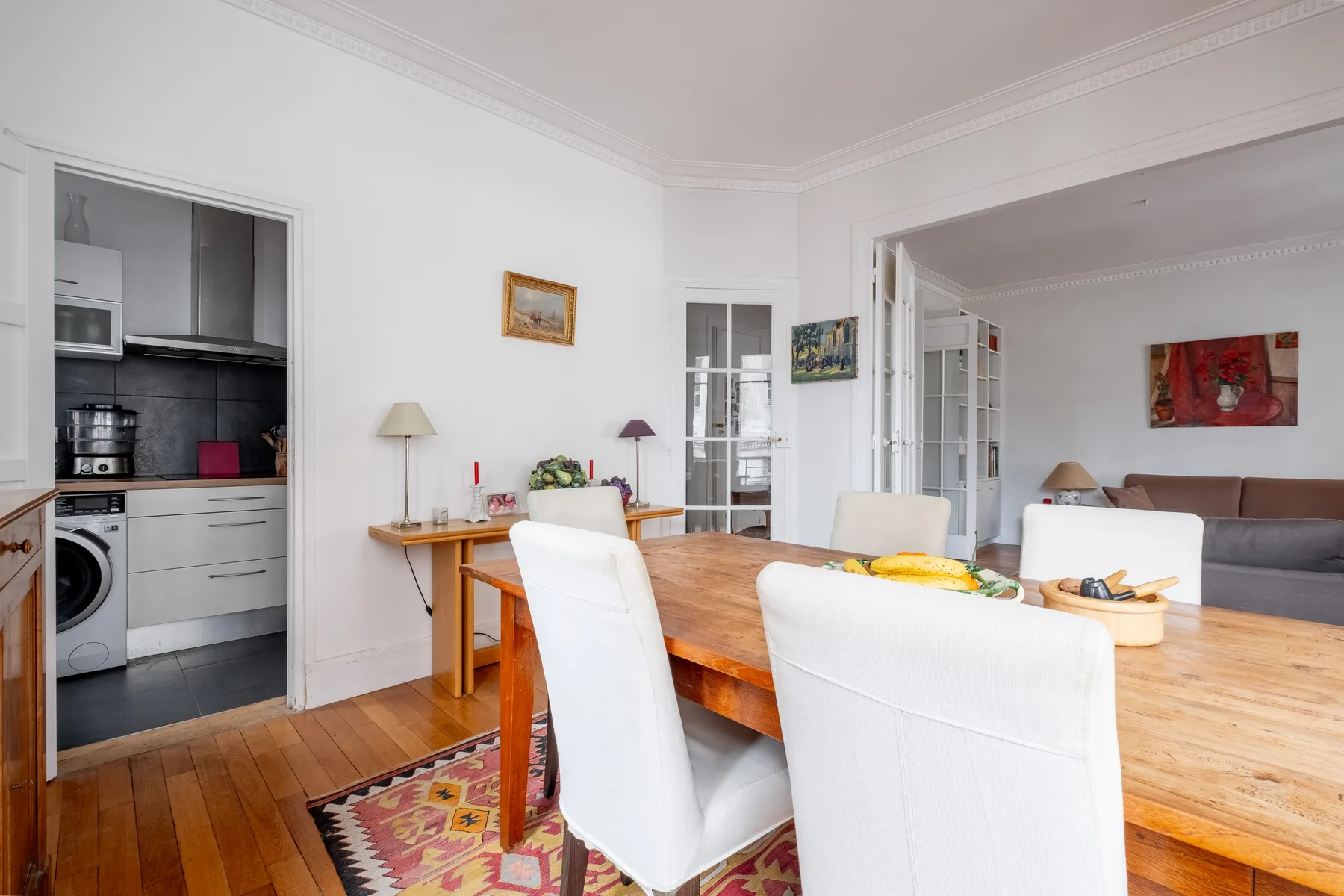 Comedor con mesa de madera y asientos blancos, junto a una cocina abierta.