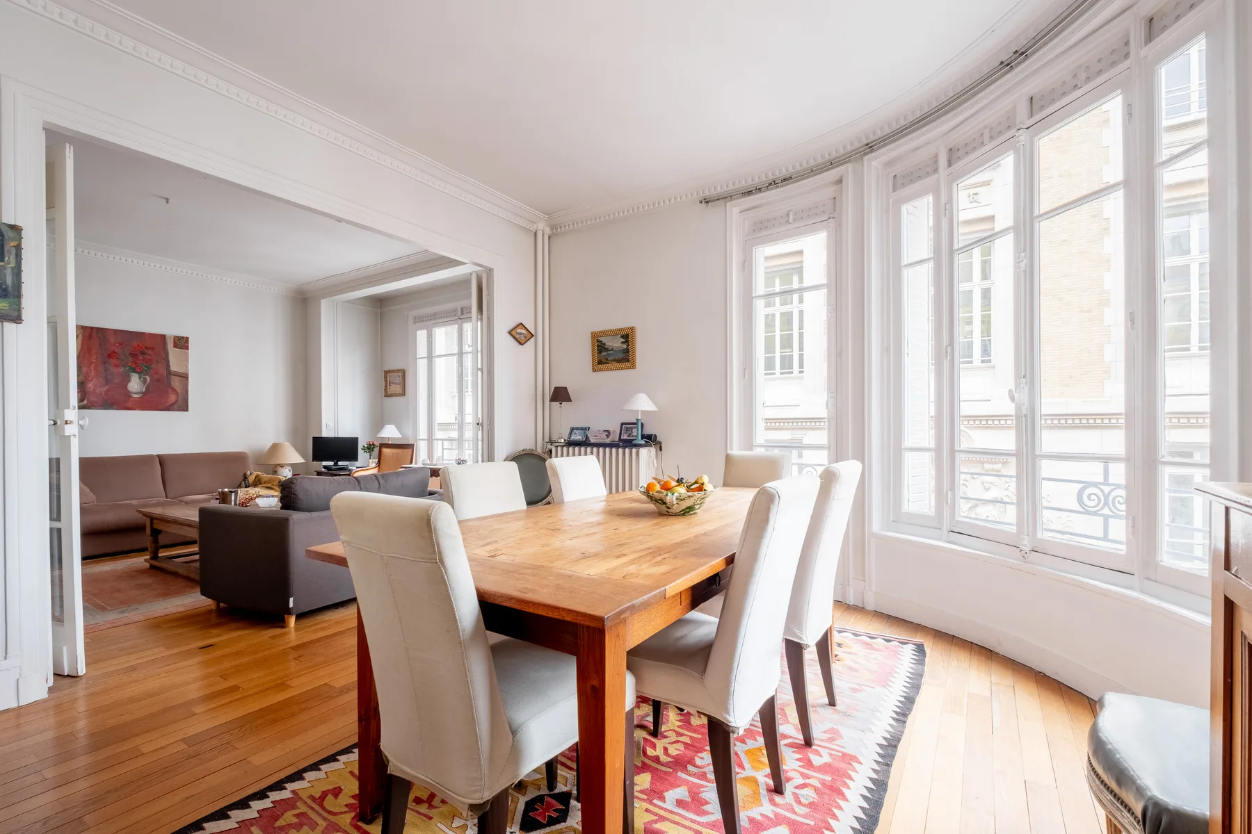 Un comedor luminoso con una mesa de madera junto a ventanas altas.