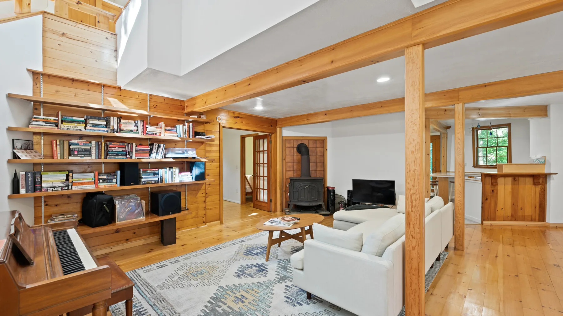 Una sala de estar con vigas de madera, estanterías, asientos y un piano.