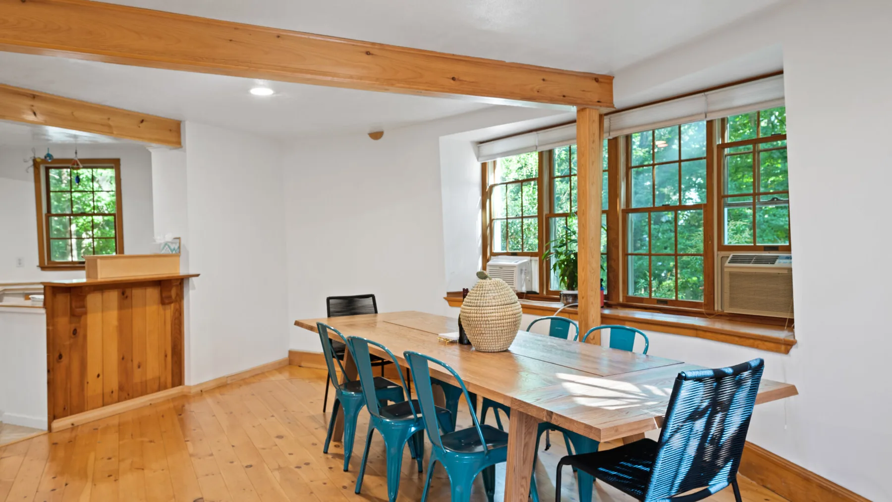 Un comedor tiene una mesa larga de madera, asientos azules y ventanas grandes.