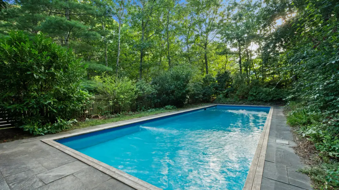 Una piscina está rodeada de caminos pavimentados y árboles frondosos.