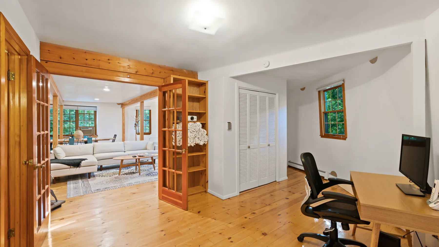 Una habitación luminosa con suelo de madera, estanterías abiertas y un escritorio junto a una zona de estar.