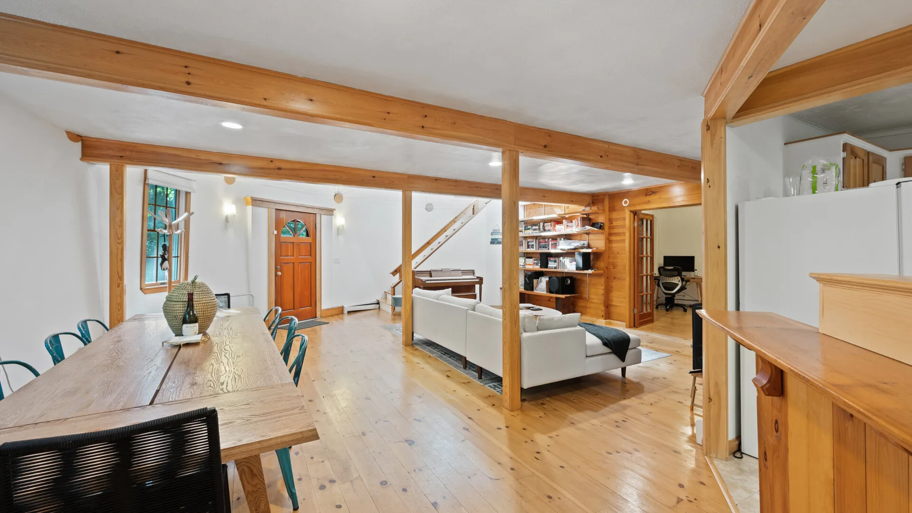 Una sala de estar y comedor de concepto abierto con vigas de madera y suelo de madera clara.