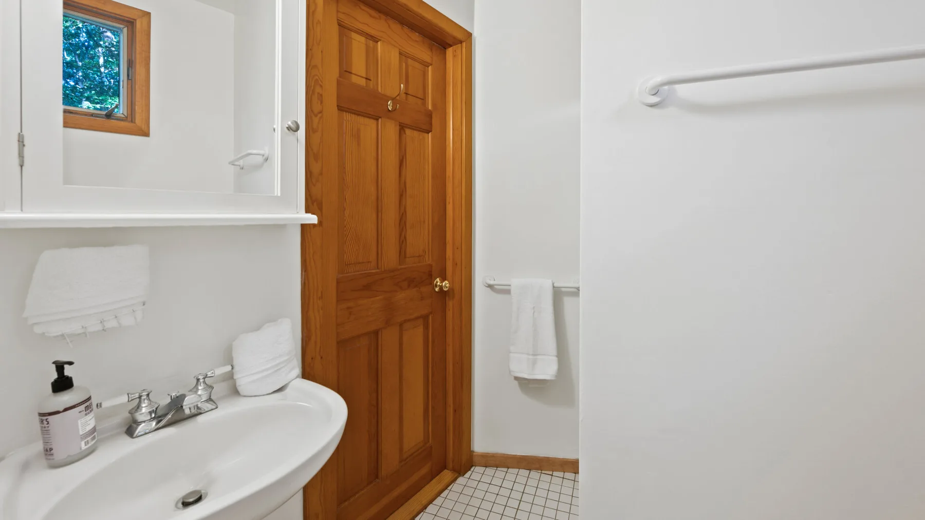 Un baño con lavabo, espejo y puerta de madera.