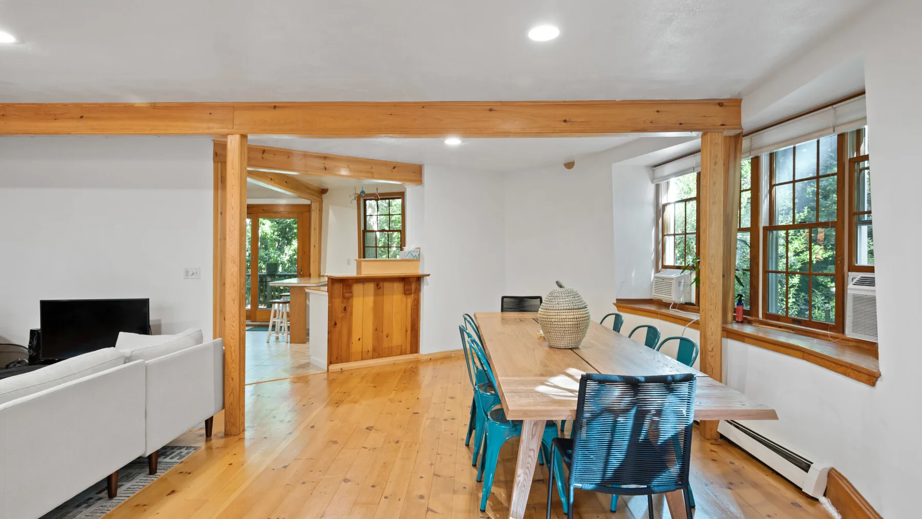 Un comedor con una mesa de madera y asientos junto a grandes ventanas.