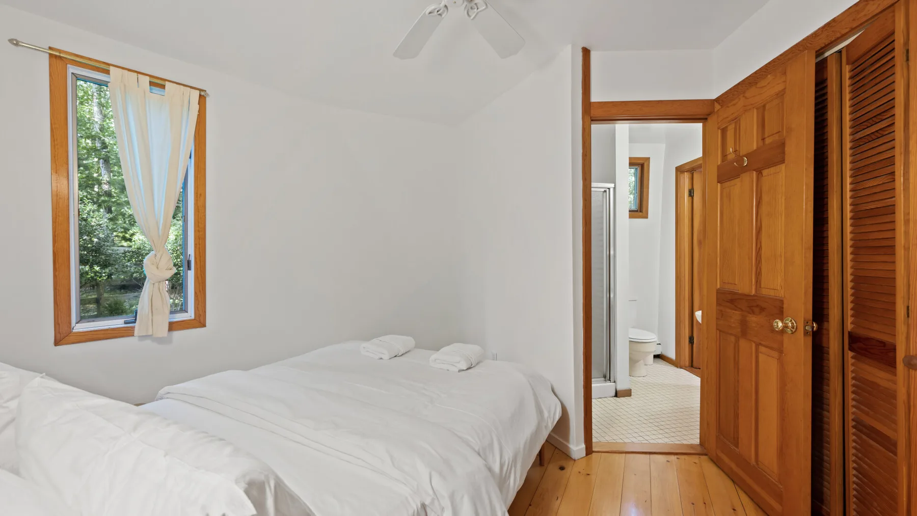 Un dormitorio luminoso con una cama tendida y una ventana con vistas a la vegetación.