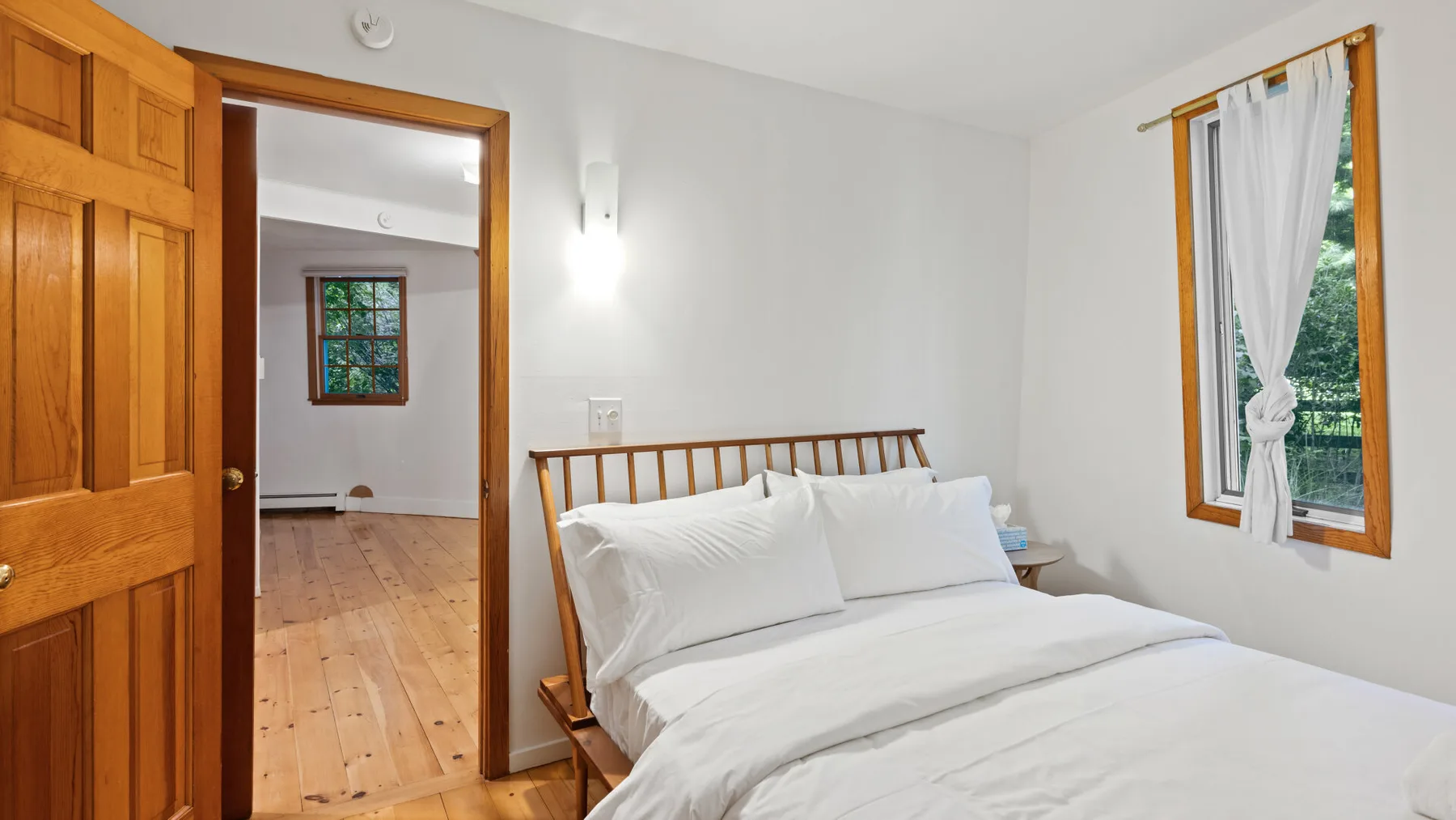 Un dormitorio con una cama de madera, ropa de cama blanca y una puerta abierta.