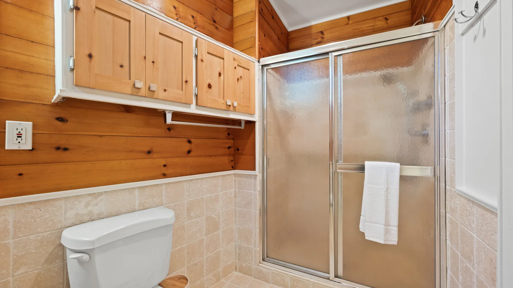 Un baño con ducha, inodoro y paredes revestidas de madera.