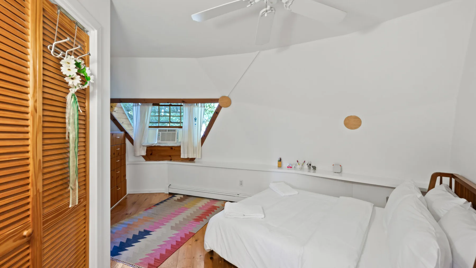 Un dormitorio luminoso con ropa de cama blanca, un ventilador de techo y una alfombra colorida.