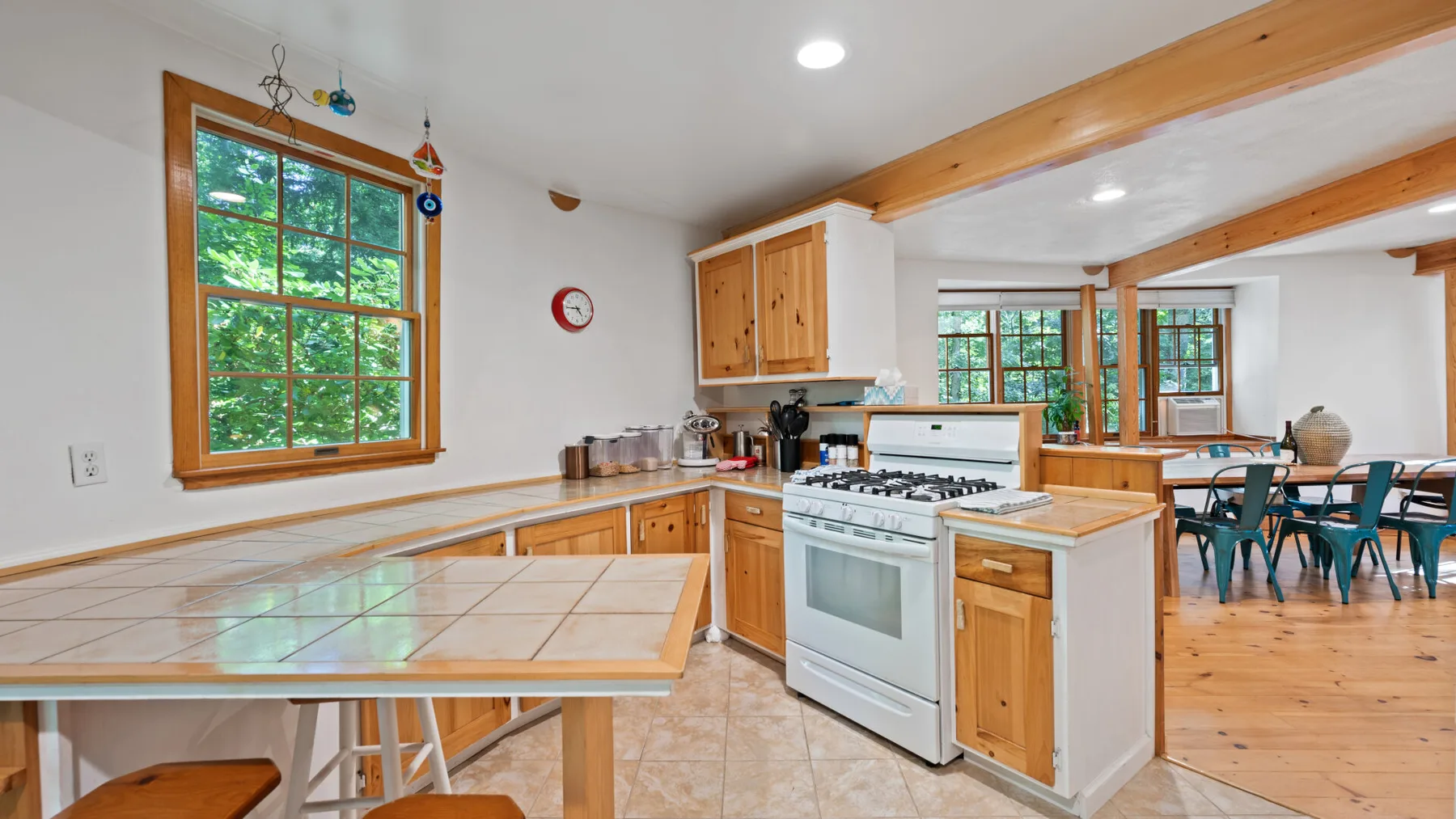 Una cocina luminosa con gabinetes de madera, una encimera de azulejos y un comedor al fondo.
