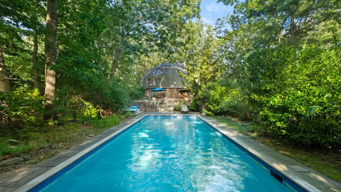 Una piscina al aire libre rodeada de árboles, con una estructura abovedada al fondo.