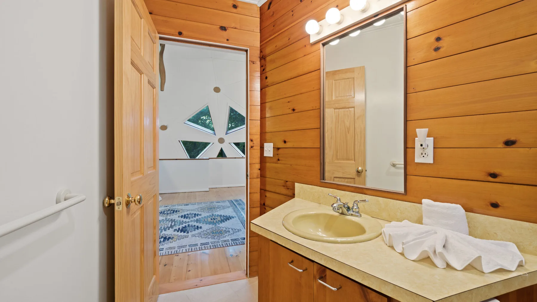 Un lavabo con espejo está junto a una pared revestida de madera.