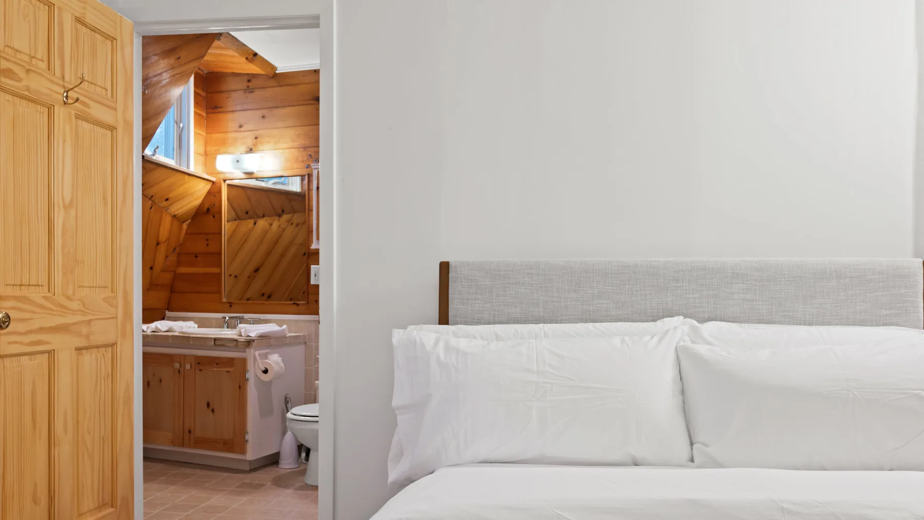 Un dormitorio con una cama junto a una puerta abierta hacia un baño revestido de madera.