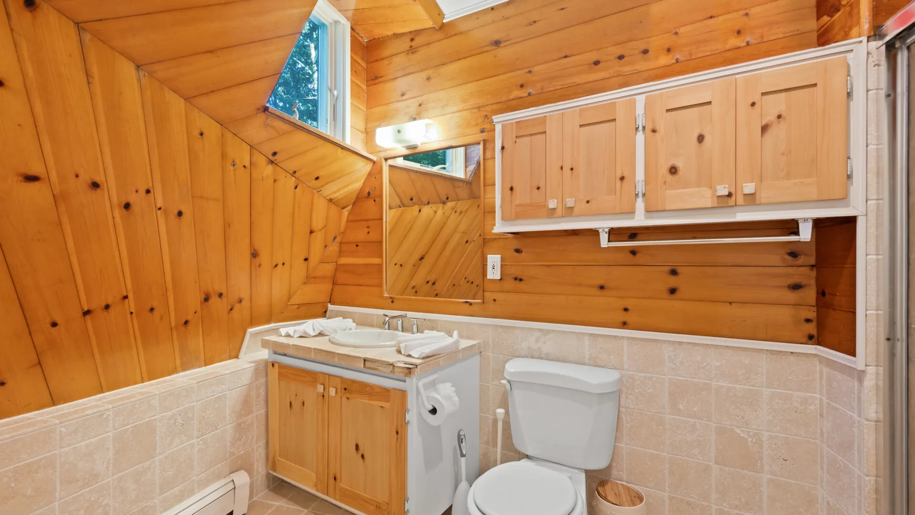 Un baño revestido de madera con lavabo, inodoro y armarios de pared.