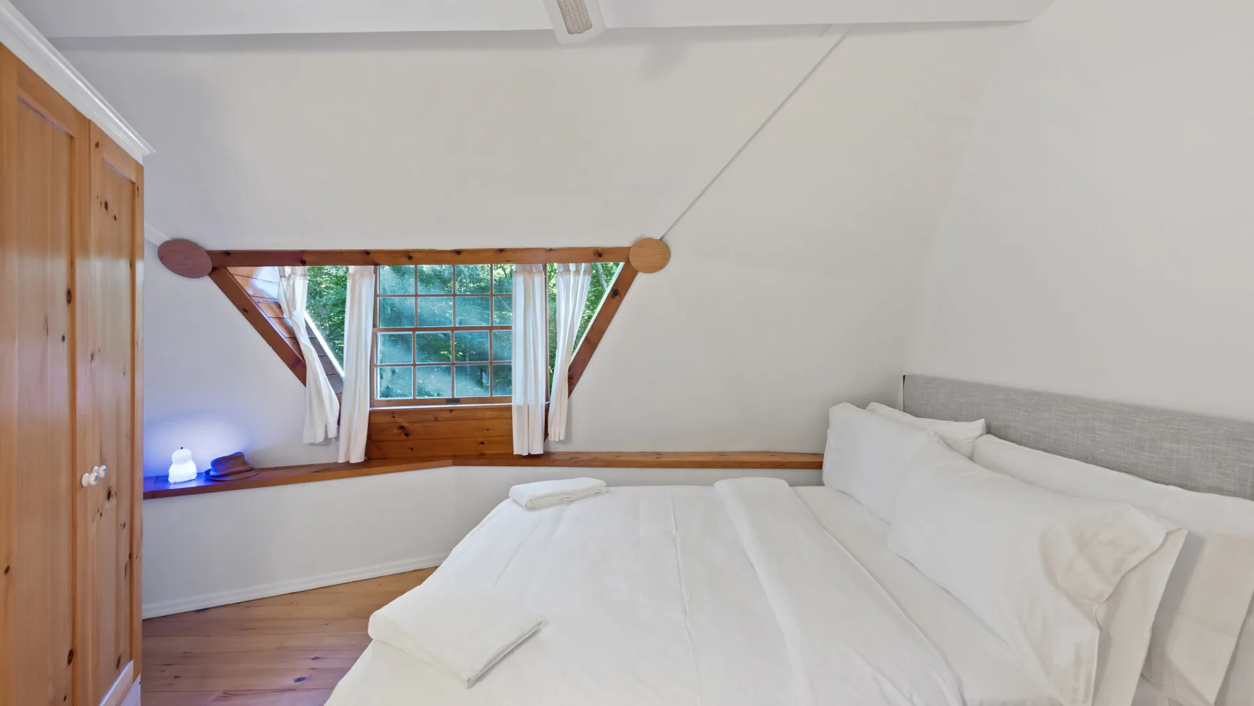 Un dormitorio luminoso con una cama blanca bajo un techo inclinado y una ventana.