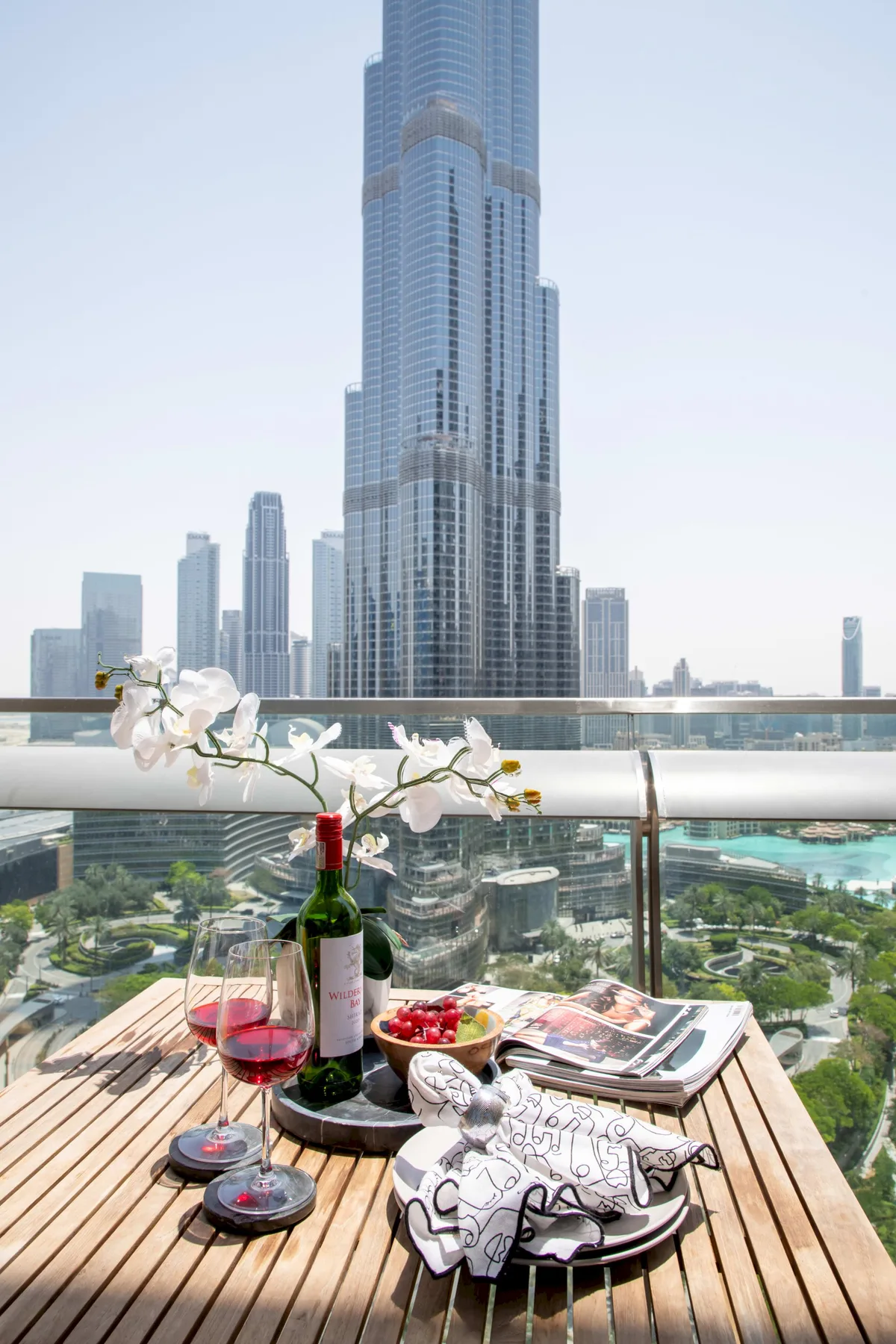 A balcony dining area overlooks a city skyline, with wine and flowers on the table.