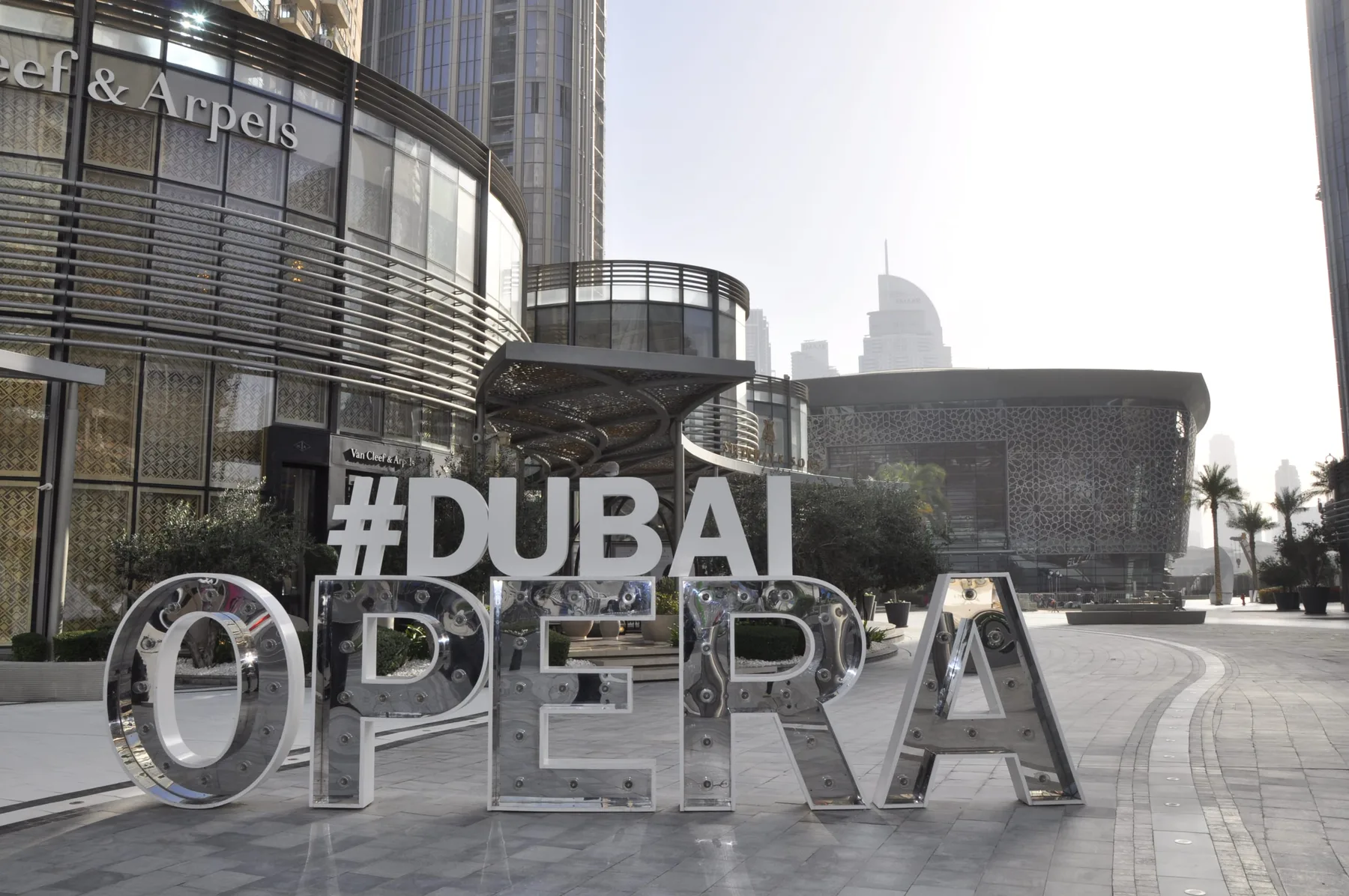 A large “#DUBAI OPERA” sign stands outside modern glass-fronted buildings.