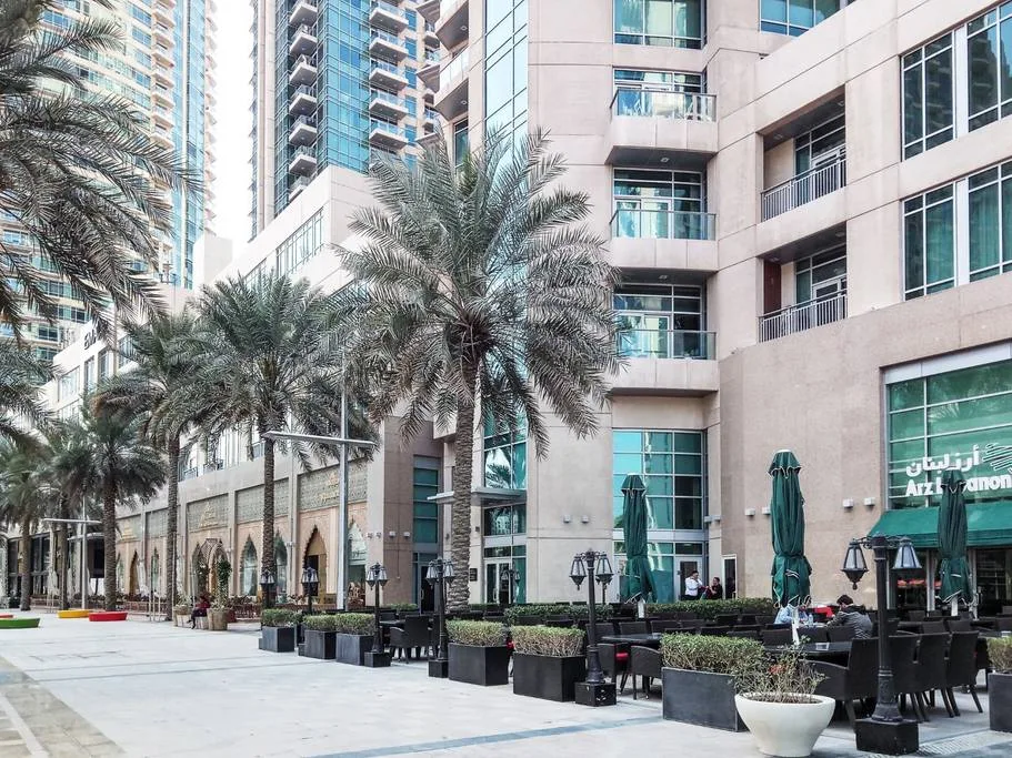 An outdoor courtyard with palm trees, planters, and seating beside a multi-story building.