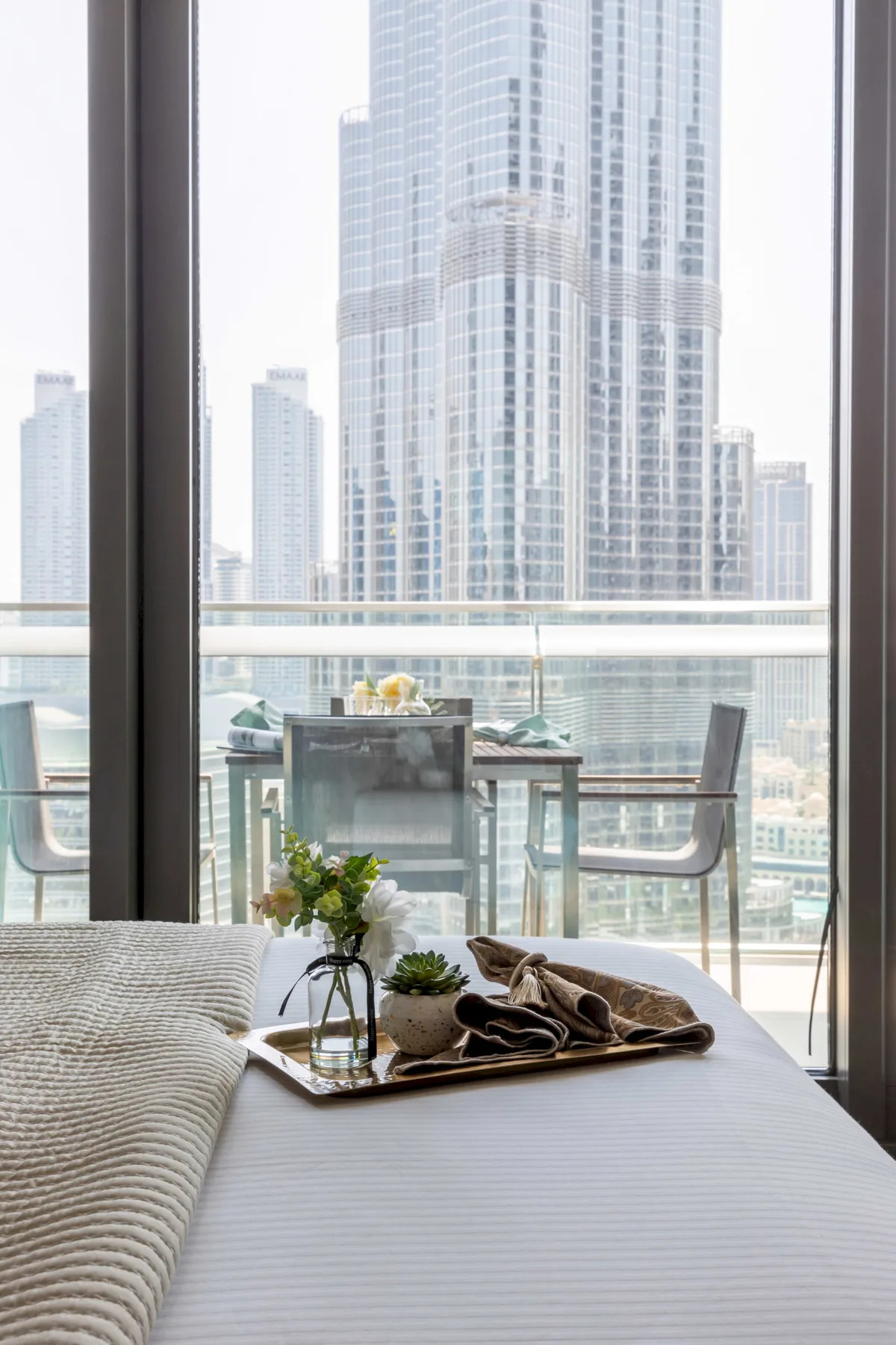 A bedroom with a neatly made bed and a view of city buildings through glass doors.