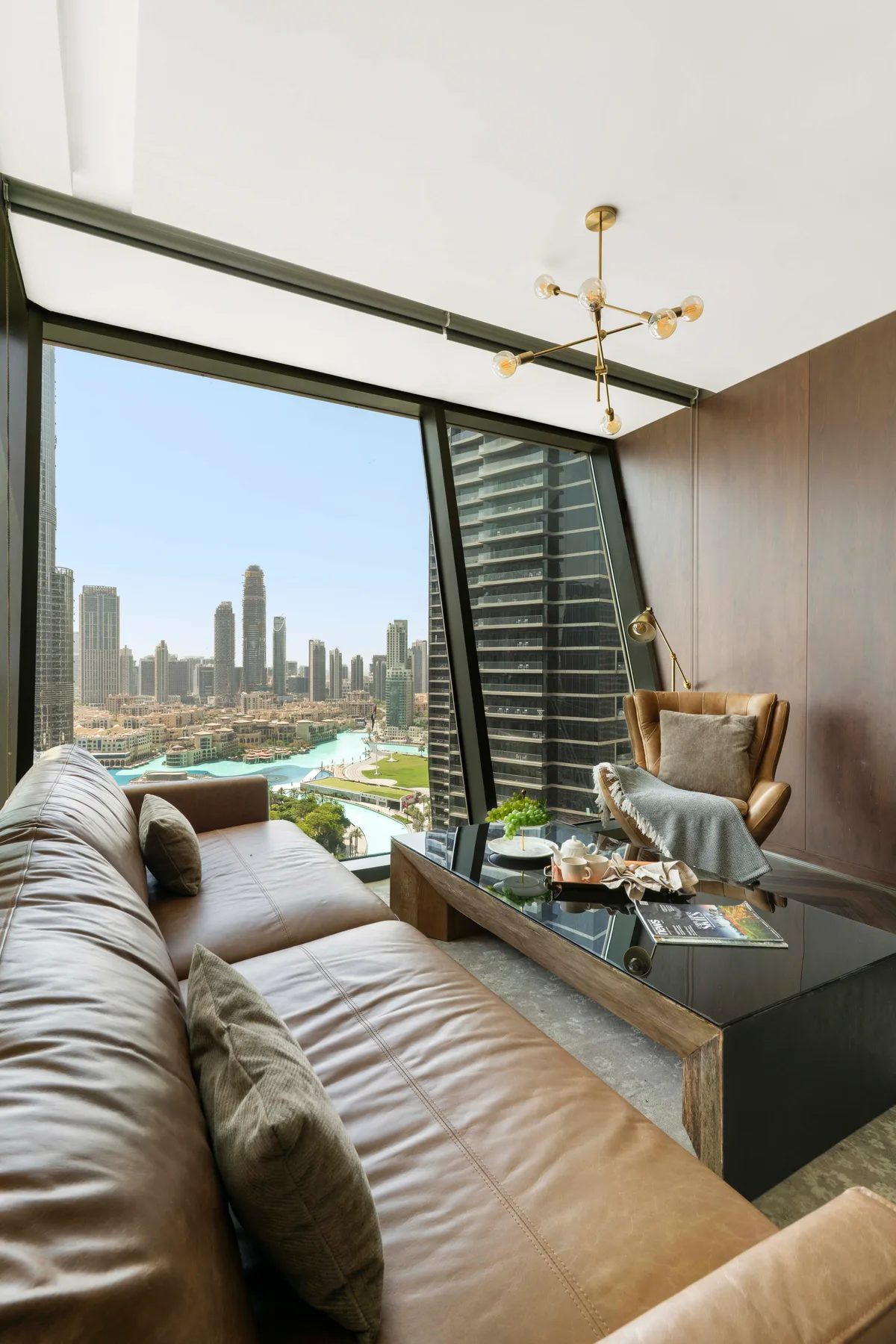 A modern living room with seating beside a large window overlooking the city.