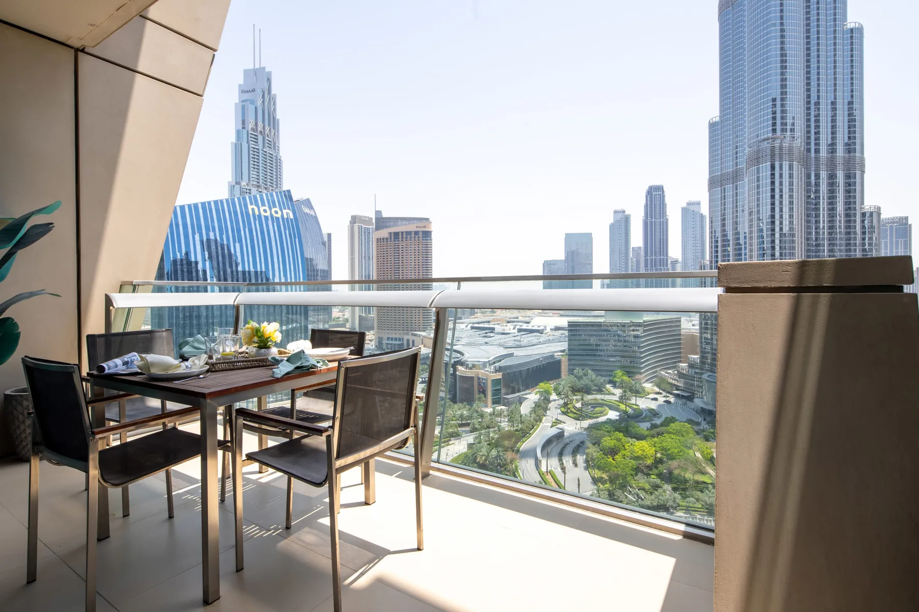 A balcony dining area overlooks a city skyline through a glass railing.