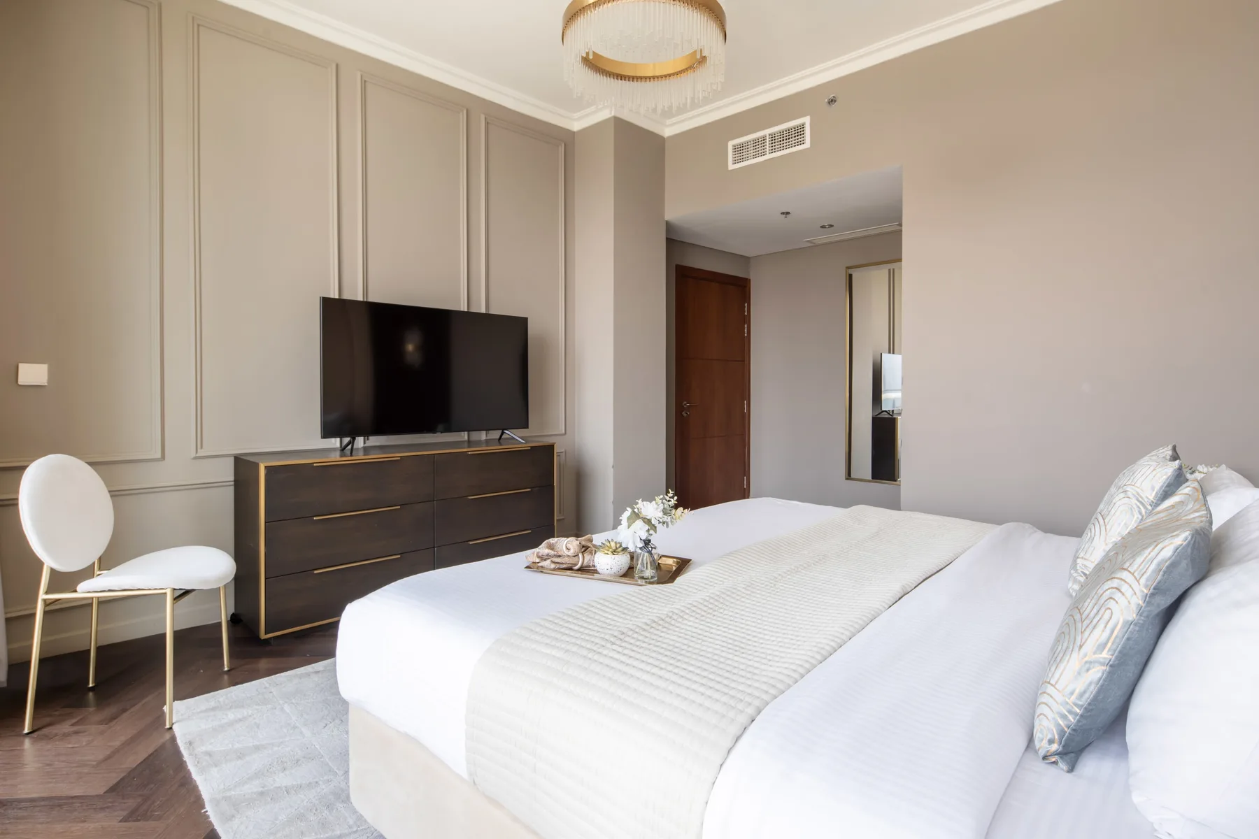A bedroom with a neatly made bed, a television, and a dark dresser.