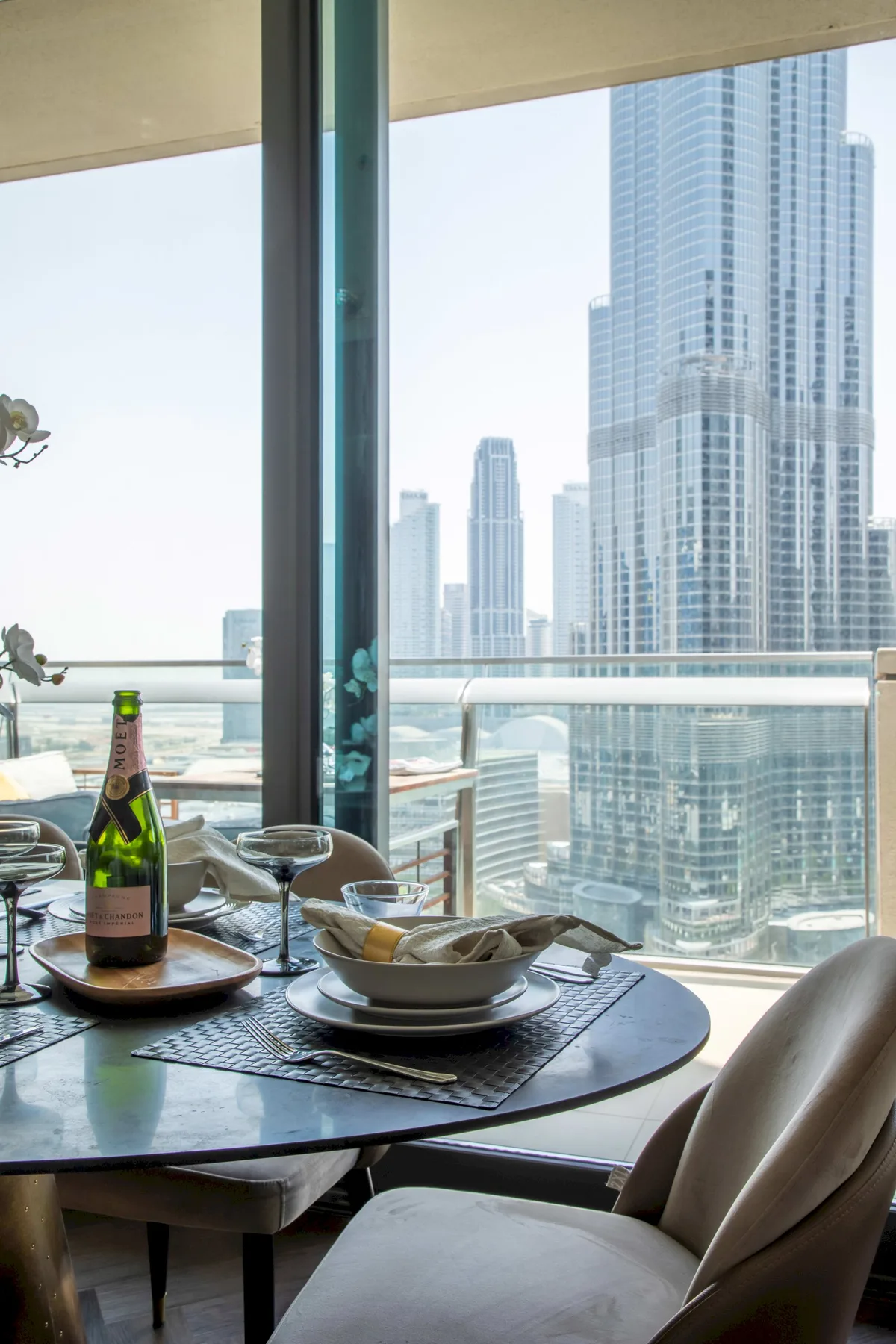 A dining table set with dishes sits beside a window overlooking city skyscrapers.