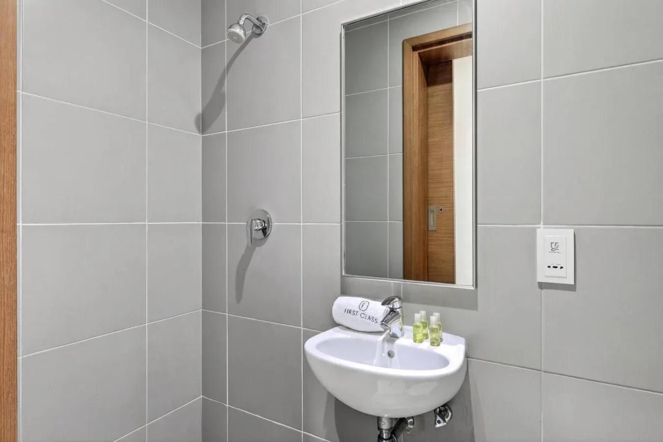 Un baño alicatado con ducha de pared y lavabo bajo un espejo.