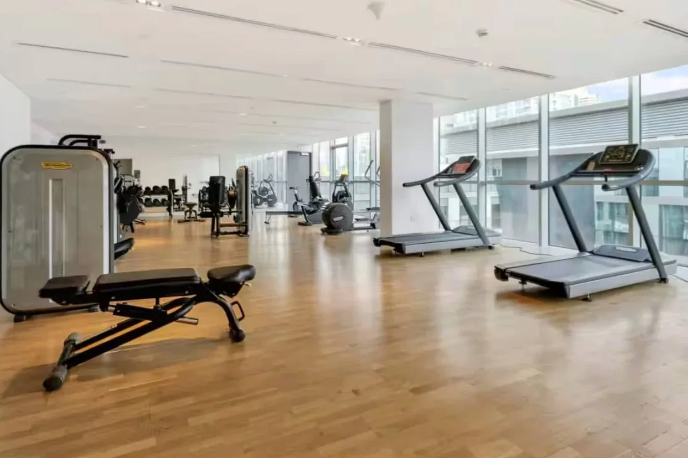 Un gimnasio amplio con máquinas de ejercicio y cintas de correr junto a grandes ventanas.