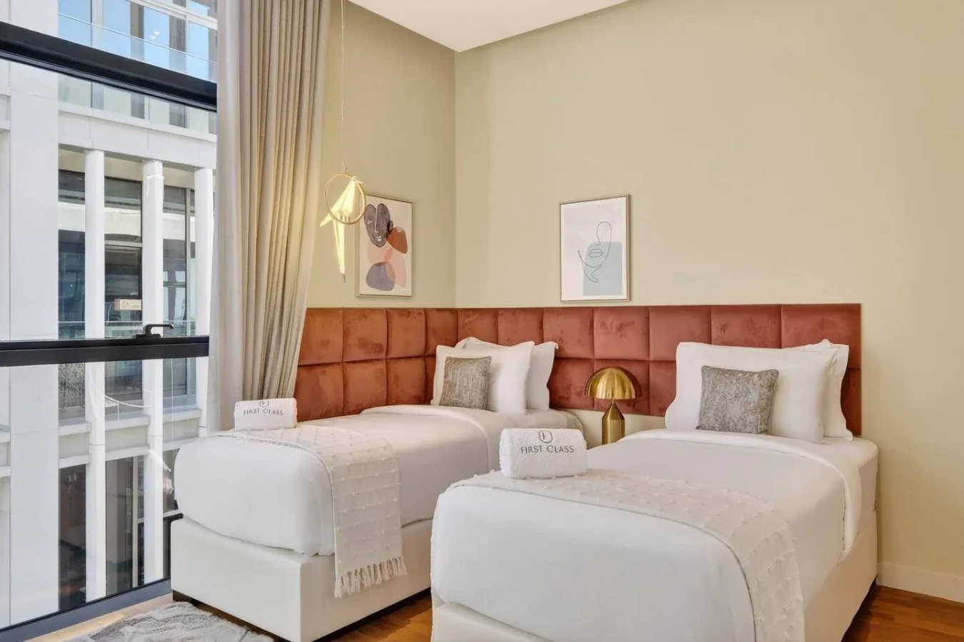 Dormitorio con dos camas y un cabecero tapizado compartido junto a una ventana grande.