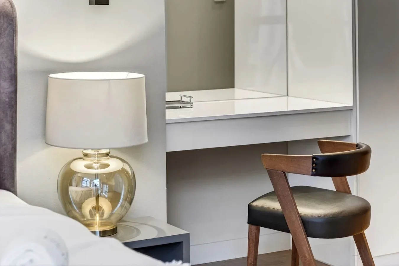 Un tocador de dormitorio con una lámpara de mesa y una silla de madera.