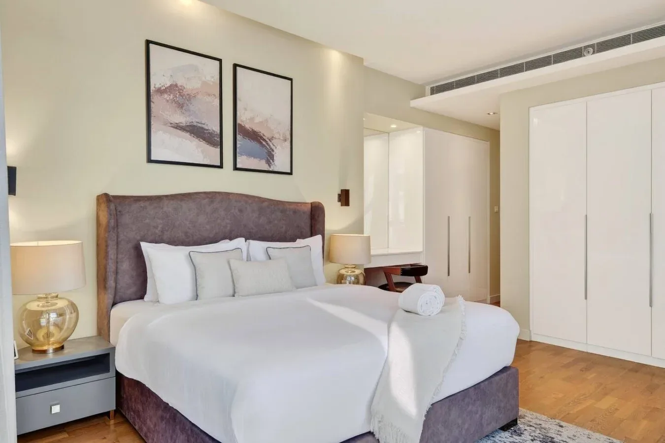 Un dormitorio con una cama bien tendida bajo dos cuadros enmarcados.