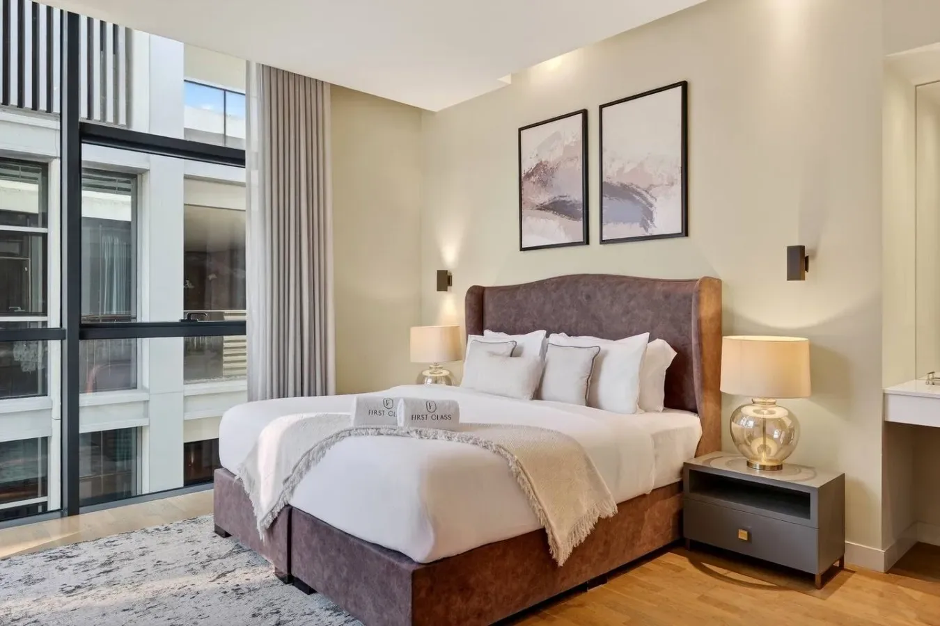Un dormitorio con una cama tendida, cuadros enmarcados y ventanas de piso a techo.