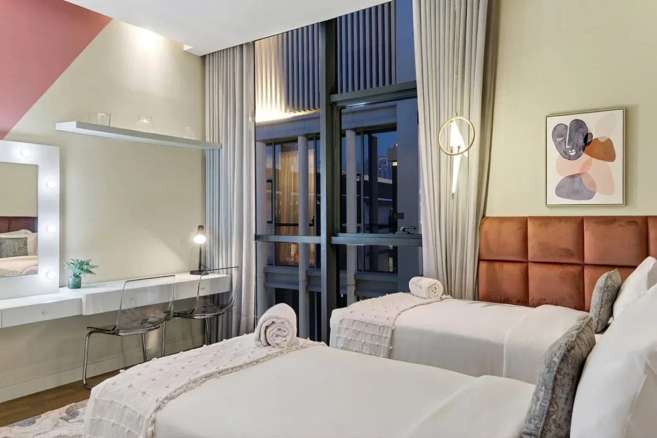 Un dormitorio con dos camas, un escritorio y ventanas altas.