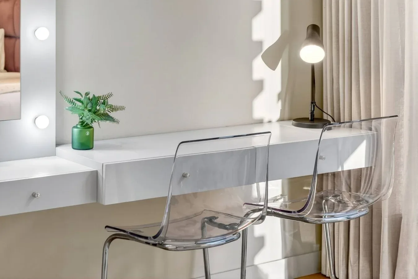 Un tocador luminoso con una encimera blanca, asientos transparentes y una pequeña planta en maceta.