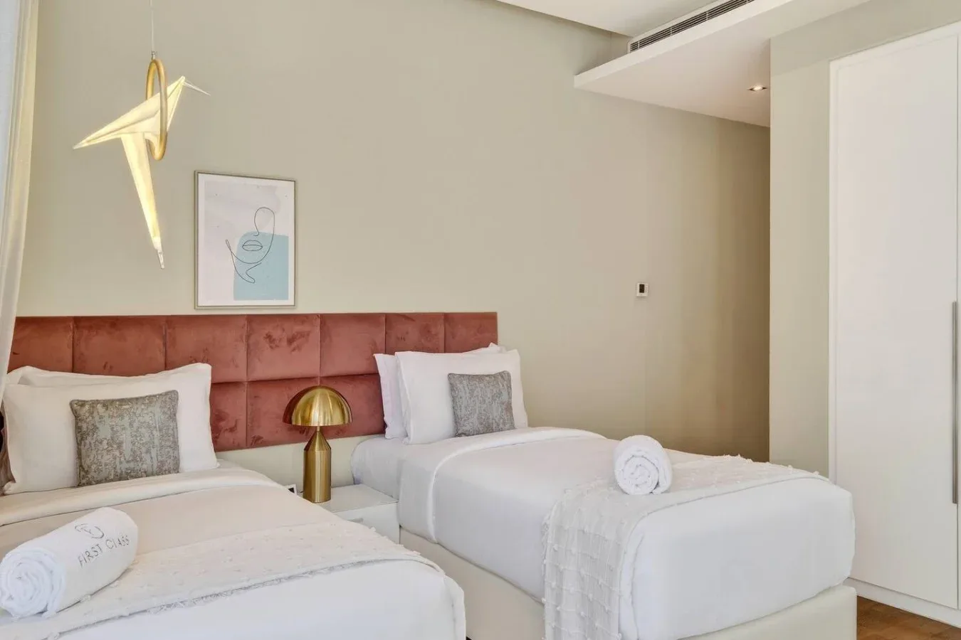 Un dormitorio con dos camas, ropa de cama blanca y un cabecero acolchado.