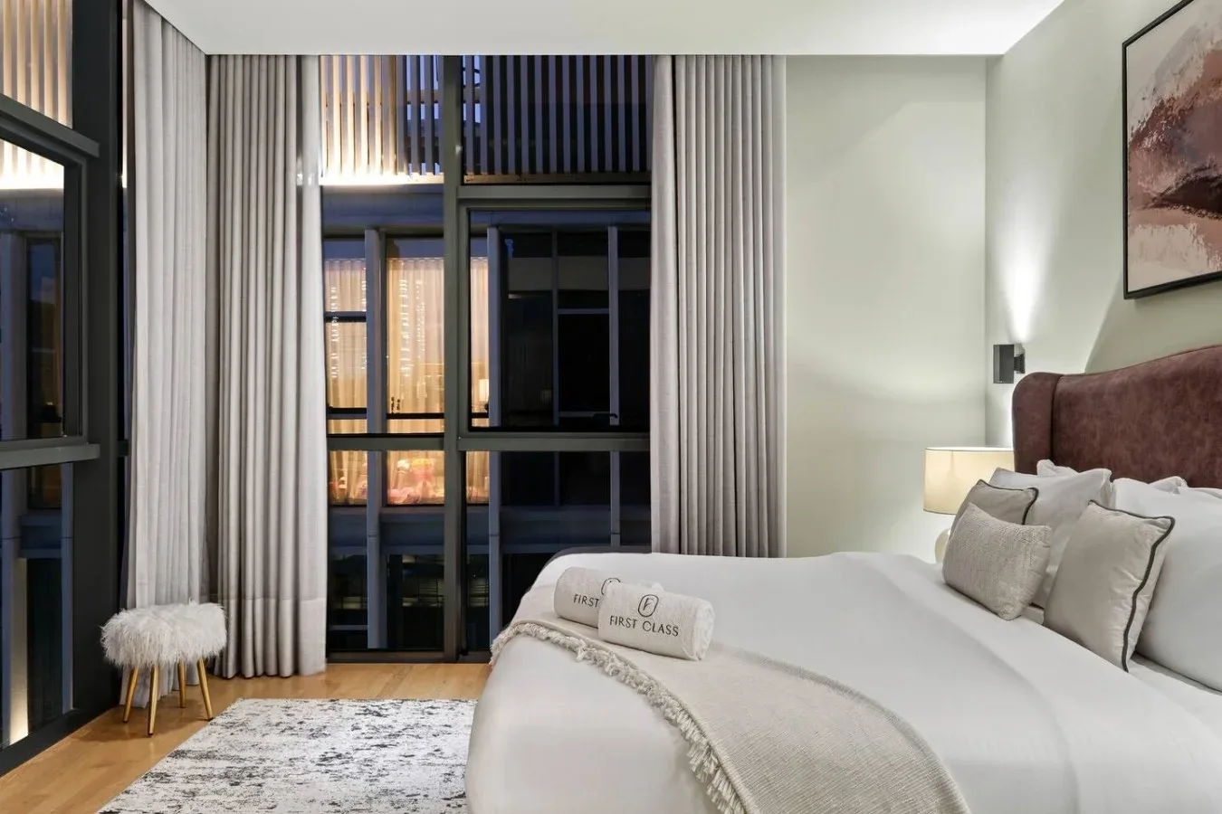 Un dormitorio con una cama grande, ropa de cama neutra y cortinas largas.