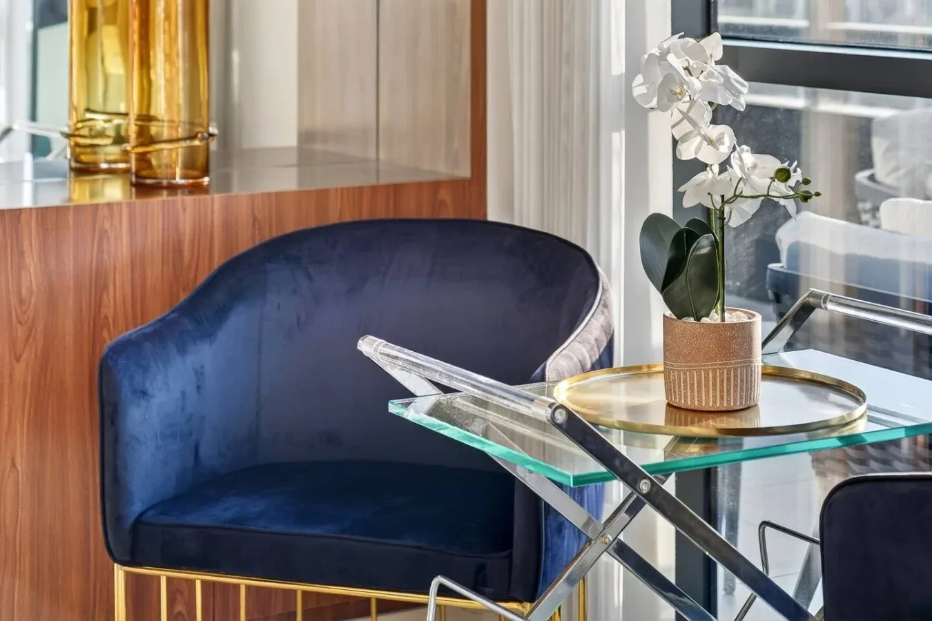 Un sillón azul está junto a una mesa de vidrio con una orquídea en maceta.