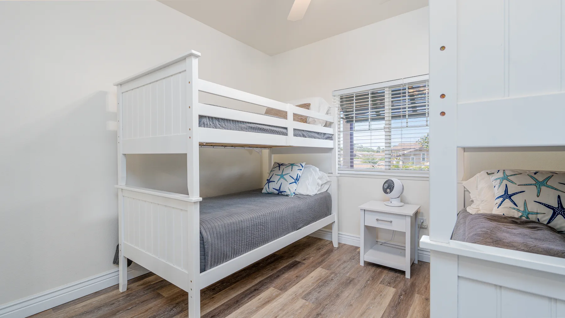 Un dormitorio luminoso con literas blancas y una ventana con persianas.