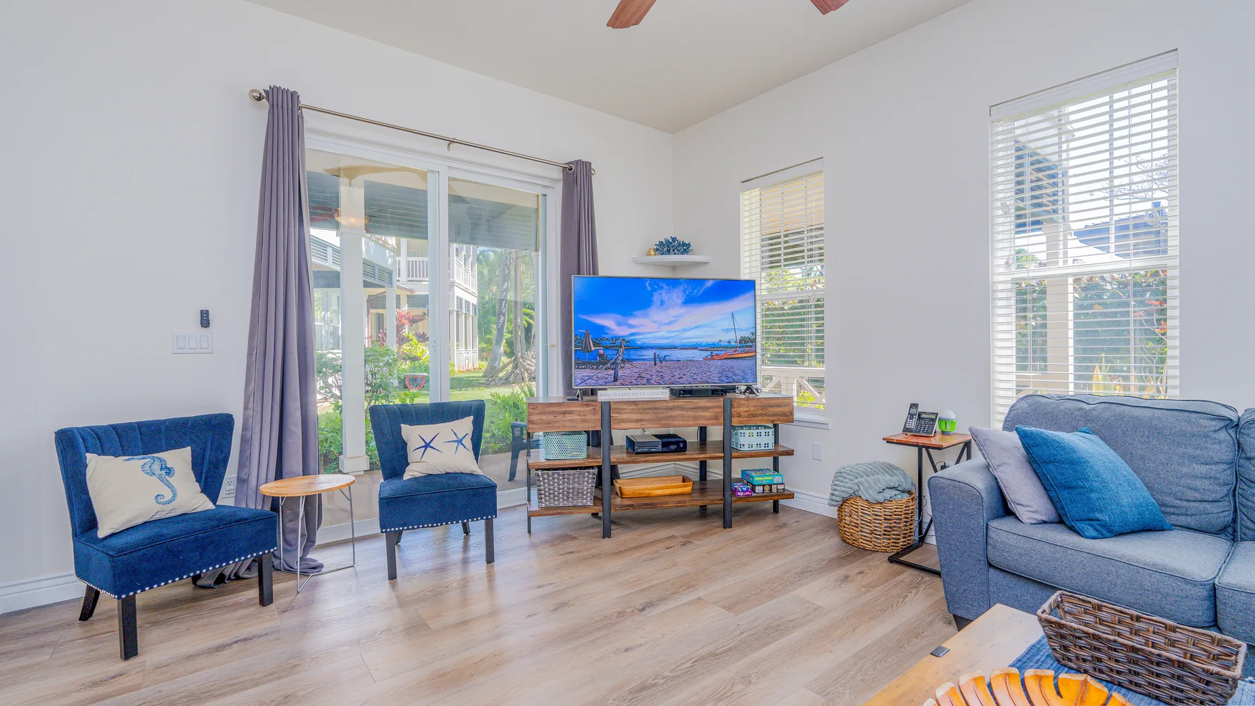 Una sala luminosa con asientos azules, un televisor y ventanas grandes.