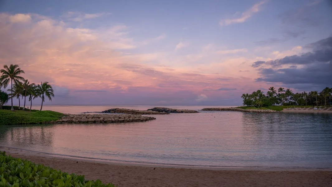 Una tranquila ensenada costera al atardecer, con palmeras junto a la orilla.