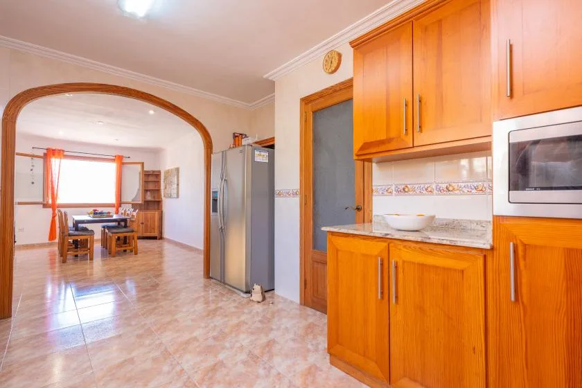 A kitchen with wooden cabinets and a refrigerator opens onto a dining area.